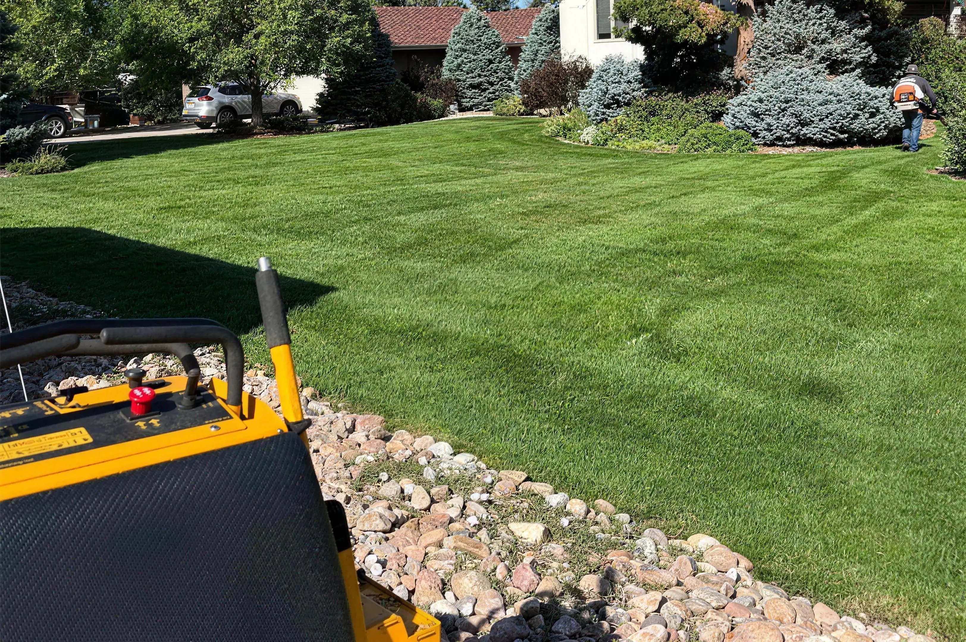 Freshly mowed lawn with mowing stripes, a mower in the foreground and a crew member clearing the edges